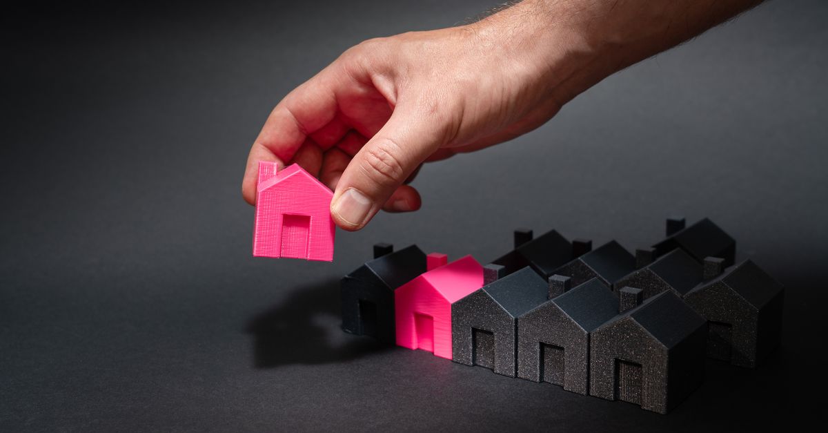 A hand selects a pink mini house among black models, symbolizing unique choice.