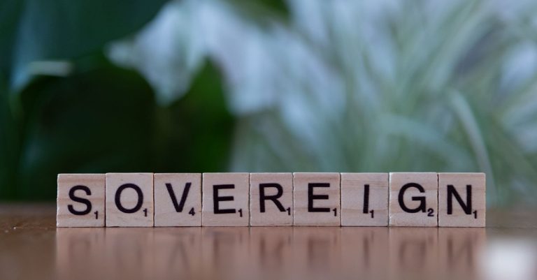 Close-up of wooden Scrabble tiles spelling 'sovereign' on a table with blurred green background.
