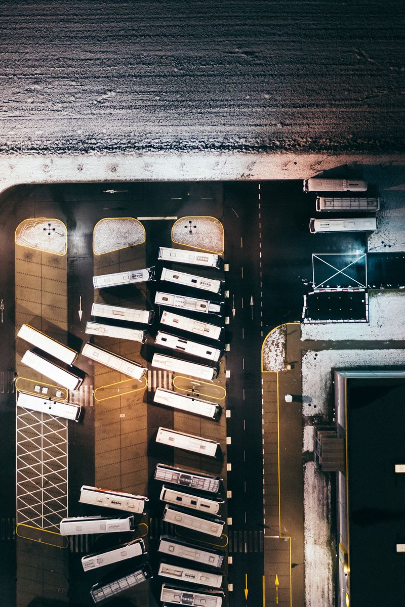 Aerial perspective of buses parked in a snow-covered depot at night, illuminated by artificial lights.
